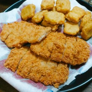 A plate of crispy fried chicken strips and nuggets served on a paper-lined dish.